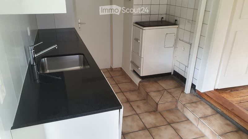 Modern kitchen with black countertop, stainless steel sink, and faucet. White cabinets and tiled floor.