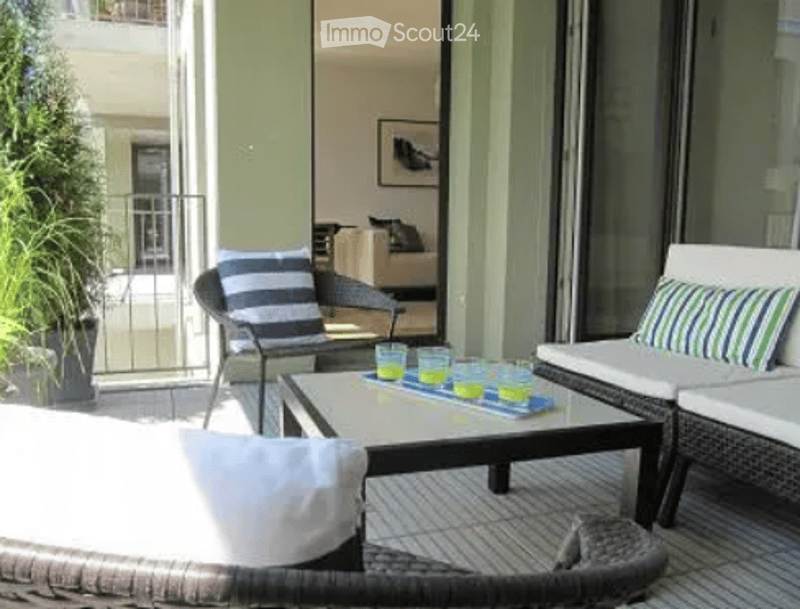 Balcony with wicker furniture, striped cushions, small table with drinks, view of another building.