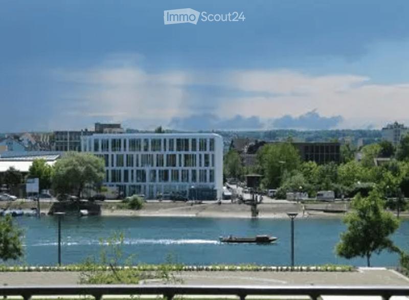 View of a river with a boat passing by, surrounded by trees and buildings on the opposite bank.