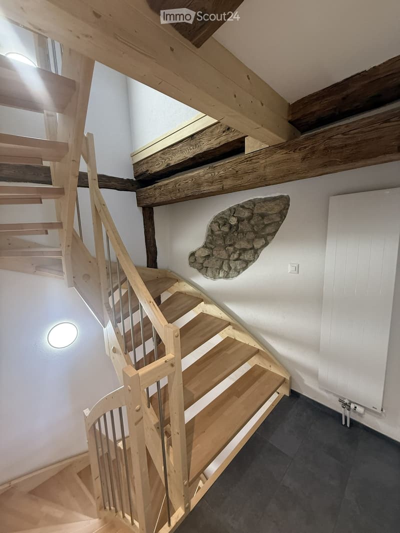 Spiral staircase with wooden steps and handrail, white walls, exposed wooden beams, and a stone wall accent.