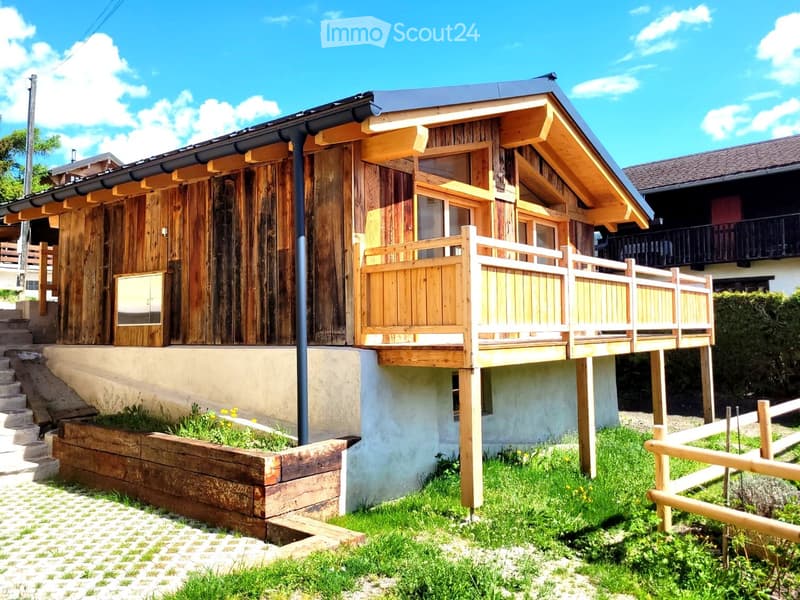 Wooden chalet with a balcony, steps leading up, and a small garden area.