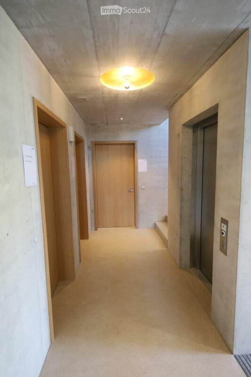 Modern hallway with light-colored walls, wooden doors, and a recessed ceiling light.