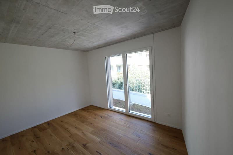 Empty room with wooden flooring, white walls, and a large sliding glass door leading to a balcony.