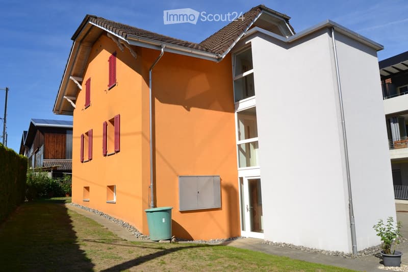 Two-story house with orange and white exterior, red shutters, and a small garden area.