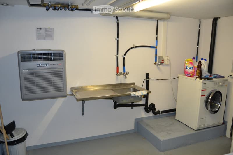 Utility room with a washing machine, sink, air conditioner, and various cleaning supplies.