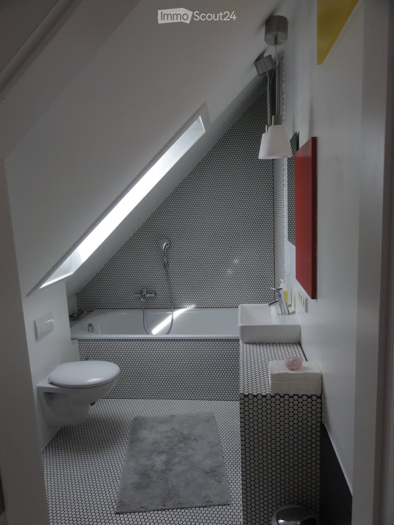 Modern bathroom with a skylight, white fixtures, and patterned tiles. Features a bathtub, toilet, sink, and a towel on the floor.