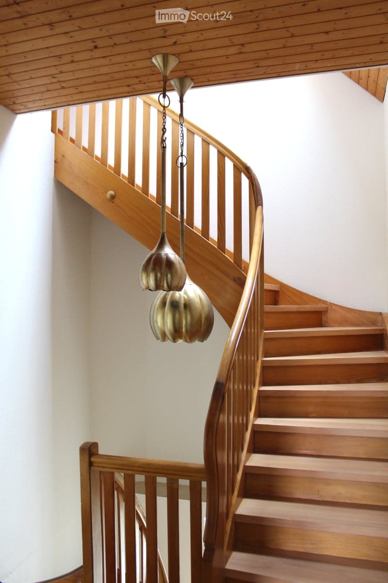 Spiral wooden staircase with a polished wooden railing and a modern pendant light fixture hanging from the ceiling.