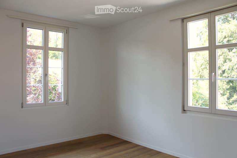 Empty room with white walls, wooden floor, and large windows with white frames. No furniture or equipment visible.