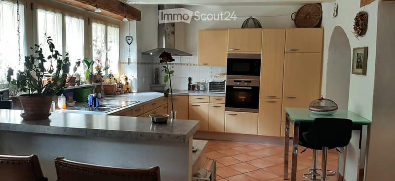 Bright kitchen with light wooden cabinets, stainless steel appliances, a central island, and a small dining area with stools.