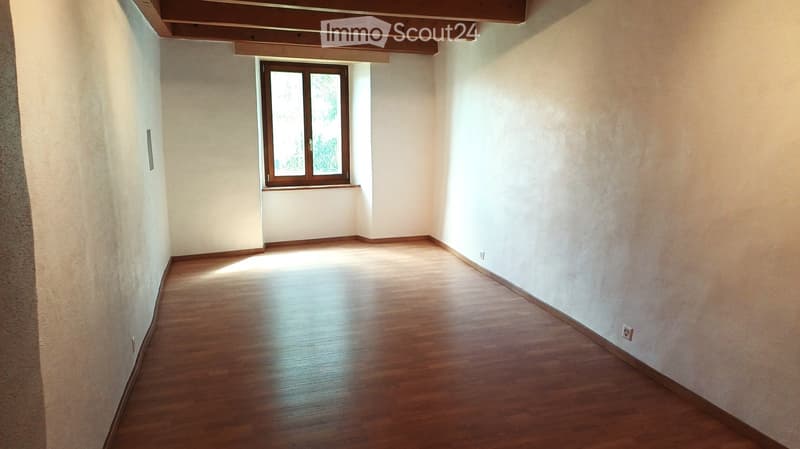 Empty room with wooden flooring, white walls, and a single window with wooden frame. No furniture or equipment present.