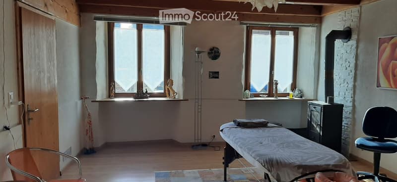 A well-lit room with wooden floors, large windows, a fireplace, and a massage table.