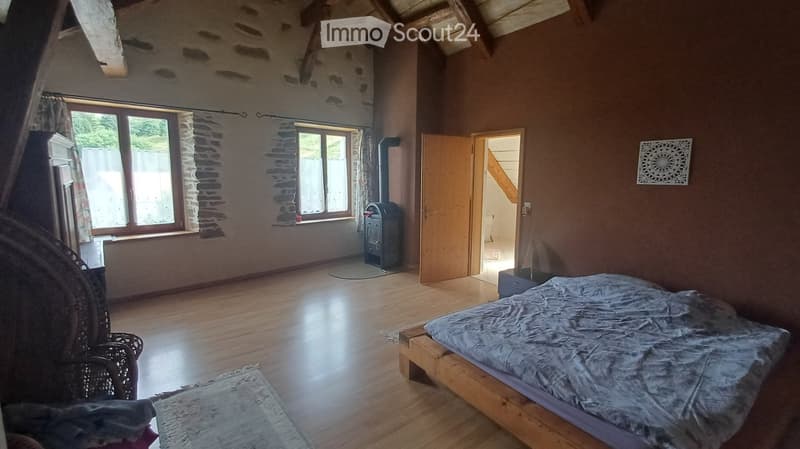 Cozy bedroom with wooden floor, bed, wicker chair, wooden door, wooden window, wooden stove, and wall decoration.