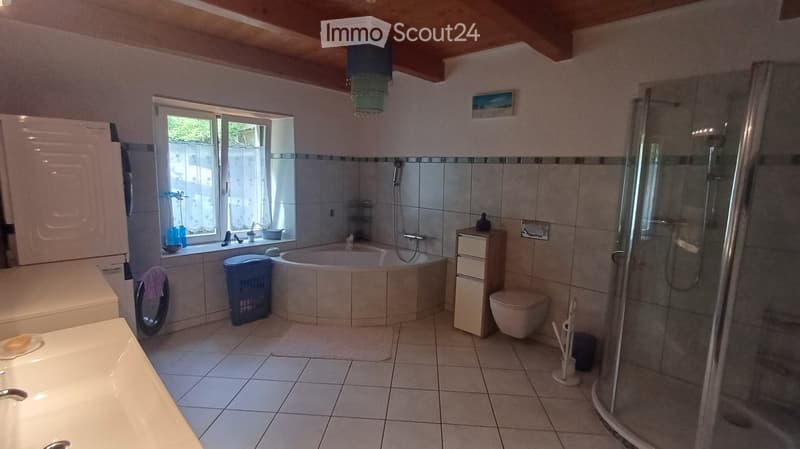Bathroom with a bathtub, toilet, sink, glass-enclosed shower, storage cabinet, and a window with a view of greenery.