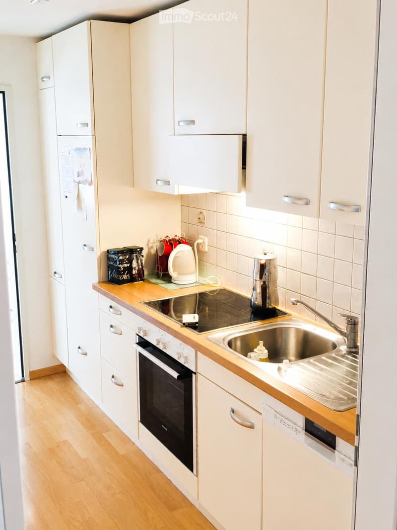 Modern kitchen with white cabinets, wooden countertops, stainless steel sink, oven, and coffee maker.