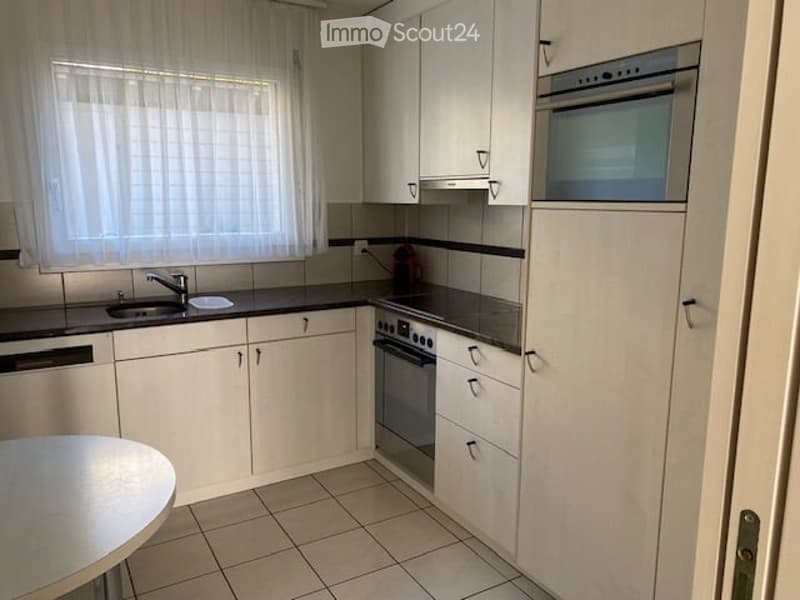 Modern kitchen with white cabinets, black countertops, and stainless steel appliances including a sink, oven, and microwave. A small round table is visible in the foreground.
