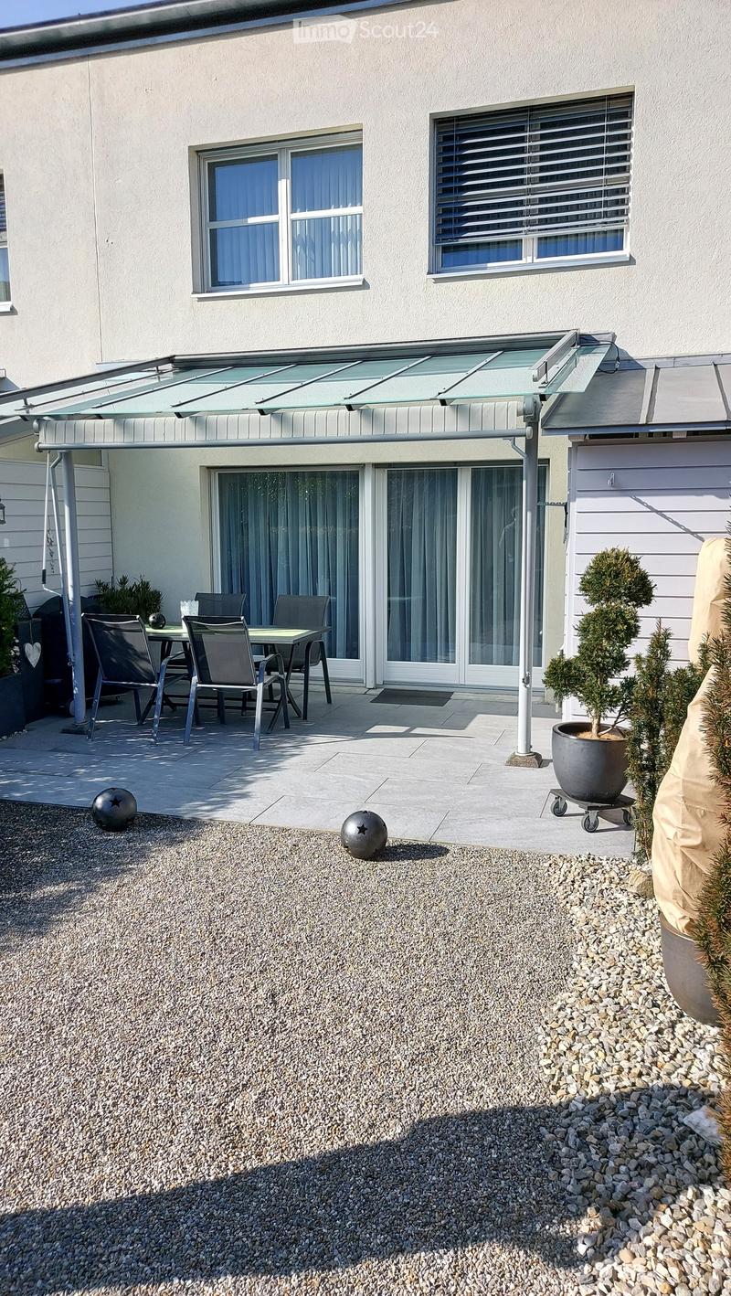 Outdoor patio area with a covered seating area, featuring a table and chairs, surrounded by gravel and potted plants.