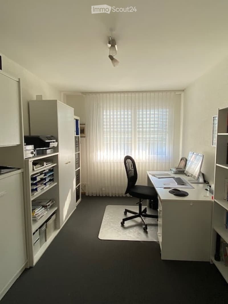 A well-organized home office with a desk, chair, laptop, bookshelf, and large window with curtains.
