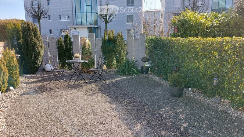 Garden area with gravel ground, small table, chairs, potted plants, and lanterns.