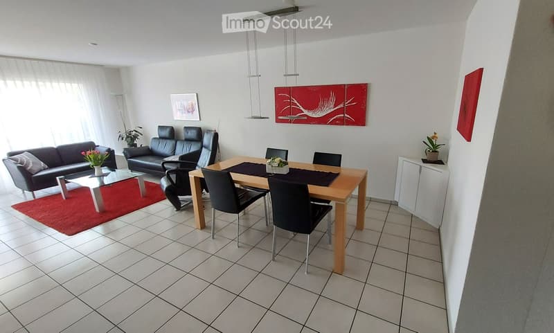Modern living and dining area with a grey sofa, coffee table, dining table with chairs, and decorative artwork on the walls.