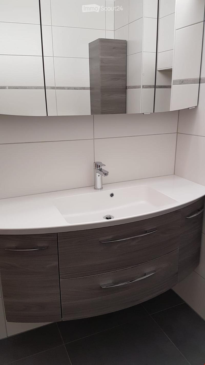 Modern bathroom with a white sink, chrome faucet, dark wooden cabinet, and large mirror with built-in storage.