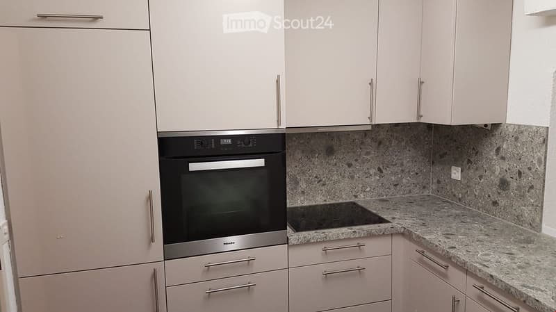 Modern kitchen with light-colored cabinets, granite countertop, and built-in oven.