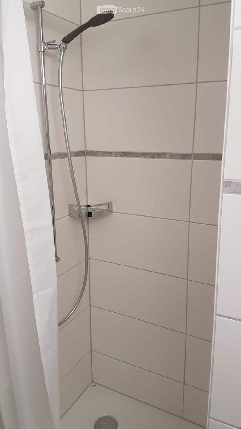 Modern shower area with white tiles, a handheld showerhead, and a sleek chrome faucet.