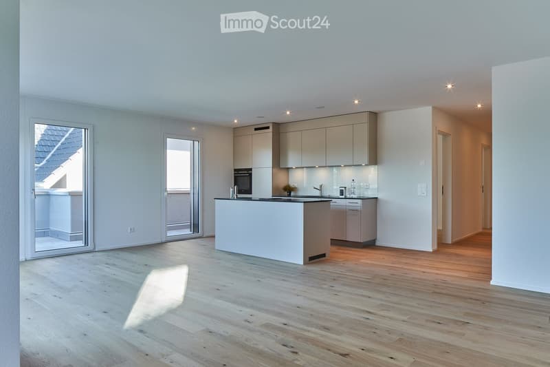 Modern kitchen with light-colored cabinets, a central island, and wooden flooring. Features include built-in appliances, ample natural light, and recessed ceiling lighting.