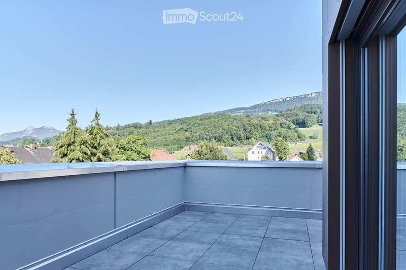 Modern balcony with tiled floor, white walls, and a panoramic view of a green landscape and mountains.