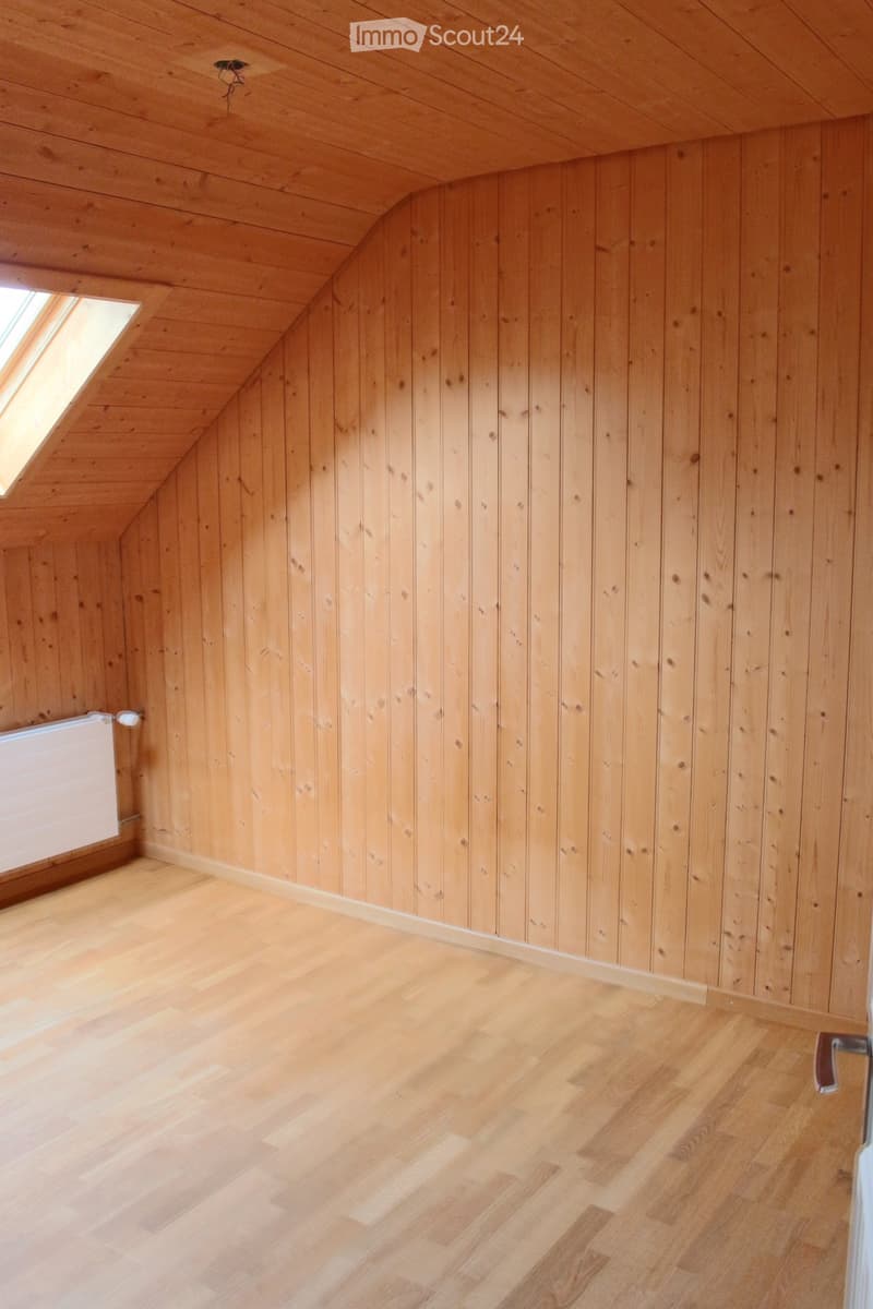 Unfurnished Room. Empty attic room with wooden walls and floor, skylight window, and a radiator on one wall.