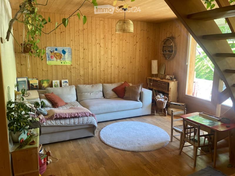 Furnished Room. Cozy living room with wooden walls and floor, featuring a sofa, small table, chairs, books, and plants.