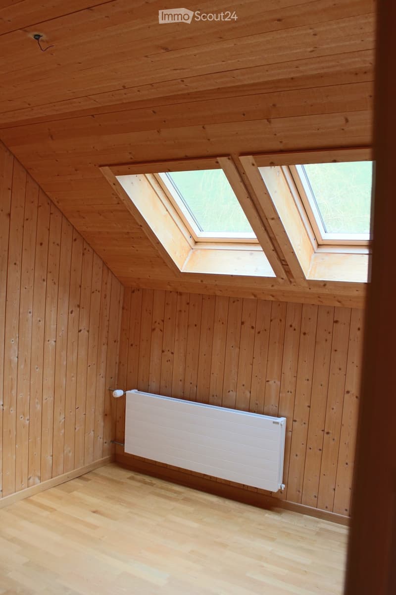 Unfurnished Room. Empty room with wooden walls, ceiling, and floor, featuring two skylight windows and a white radiator on one wall.