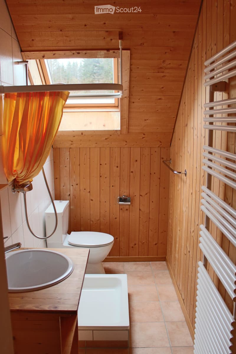 Bathroom. Cozy wooden bathroom with a sink, toilet, shower, and radiator. Features a large window with an orange curtain and wooden walls.