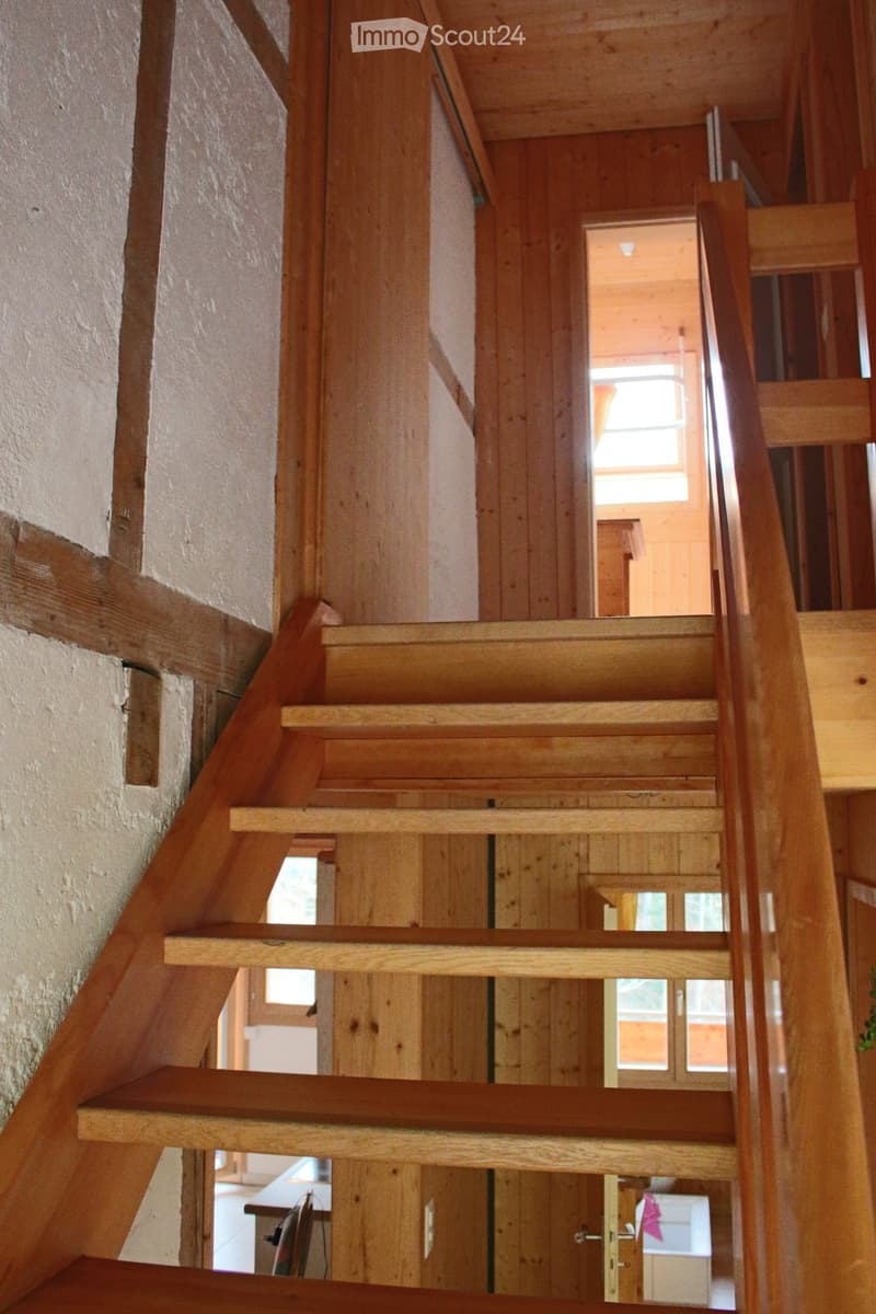 Corridor / Hallway. Wooden staircase with open wooden railings and steps, leading to an upper level with visible windows and a glimpse of a room beyond.