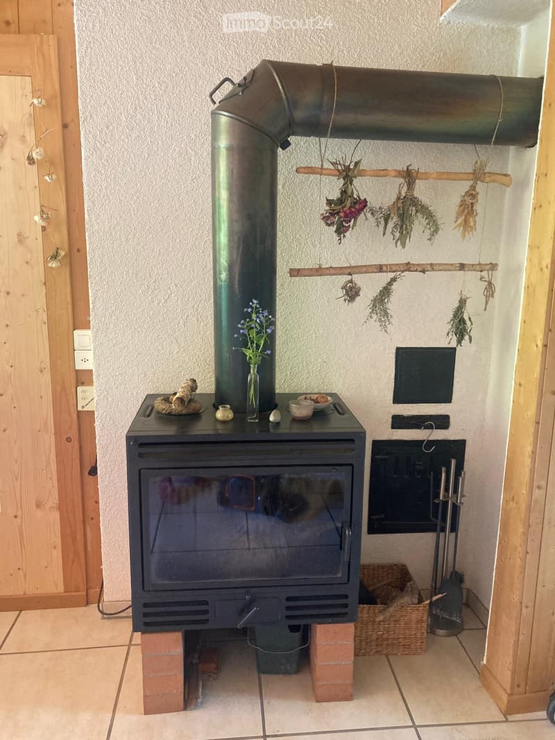 Furnished Room. A rustic fireplace with a black stove, decorative items on top, dried herbs hanging, and a small vase with flowers.