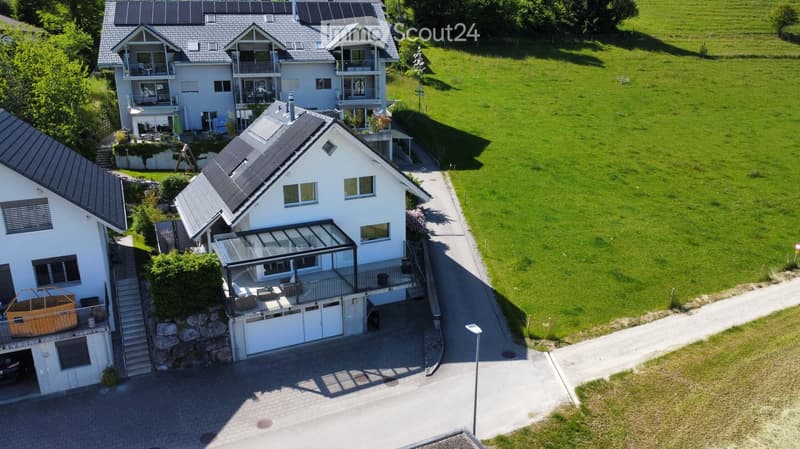 Aerial view of a modern two-story house with solar panels, garage, and spacious lawn.