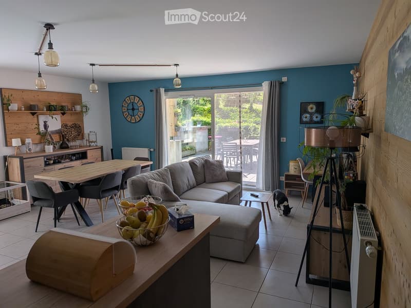 Modern living room with blue walls, grey sofa, coffee table, dining table, chairs, and a view to a patio area.