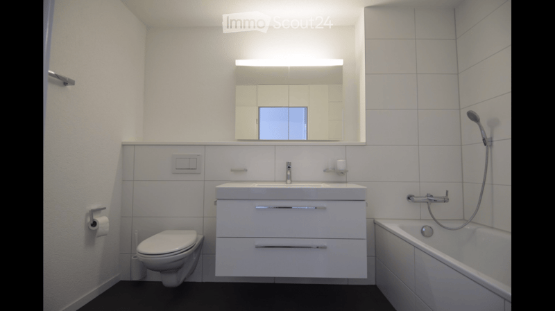 Modern bathroom with white tiles, a toilet, a sink with a mirror above it, a bathtub, and a showerhead.