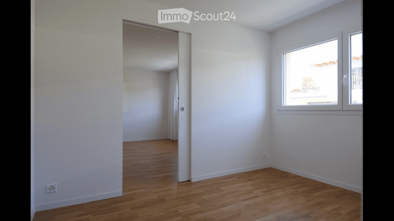 Empty room with wooden flooring, white walls, and a window with a view of a balcony. No furniture or equipment present.