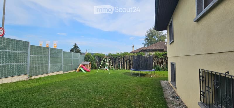Well-maintained backyard with green grass, a trampoline, swing set, small playhouse, and a privacy fence.