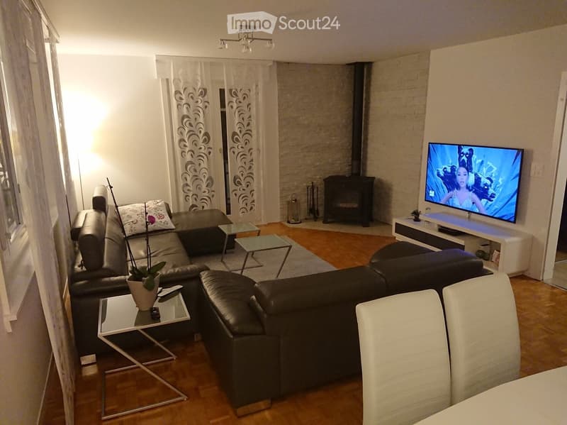 Modern living room with a black leather sectional sofa, glass coffee tables, a flat-screen TV, a fireplace, and a potted plant on a side table.