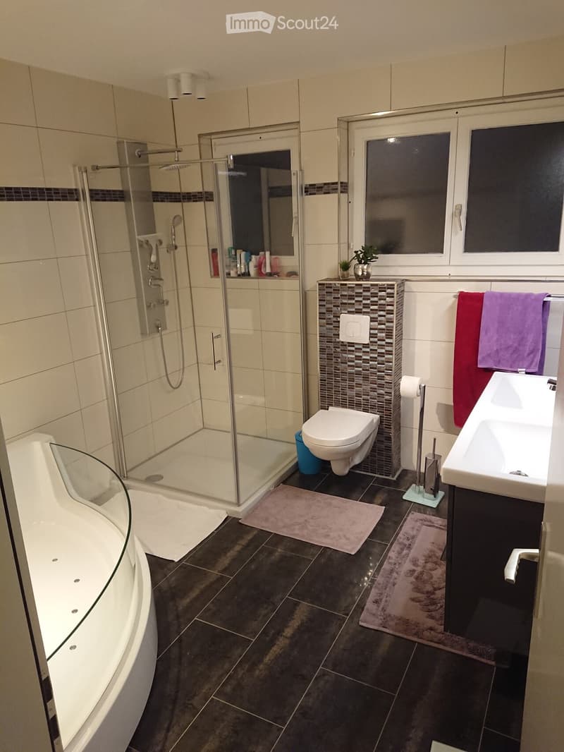 Modern bathroom with a bathtub, toilet, sink, and walk-in shower. Features include dark tiled flooring, white walls, and a decorative mosaic tile backsplash around the sink area.