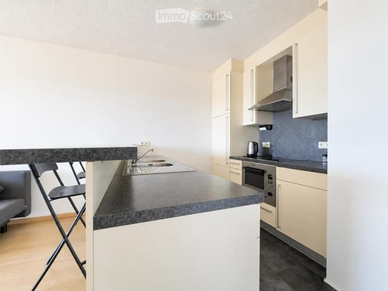 Modern kitchen with white cabinets, black countertops, and stainless steel appliances. Features a central island with a sink and a chair tucked under it.