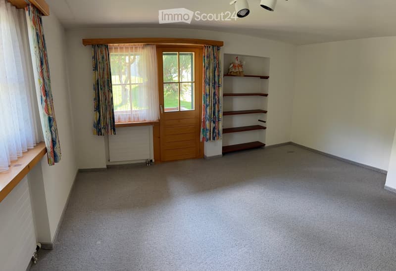 Empty room with carpeted floor, wooden door, built-in shelving unit, and windows with curtains.