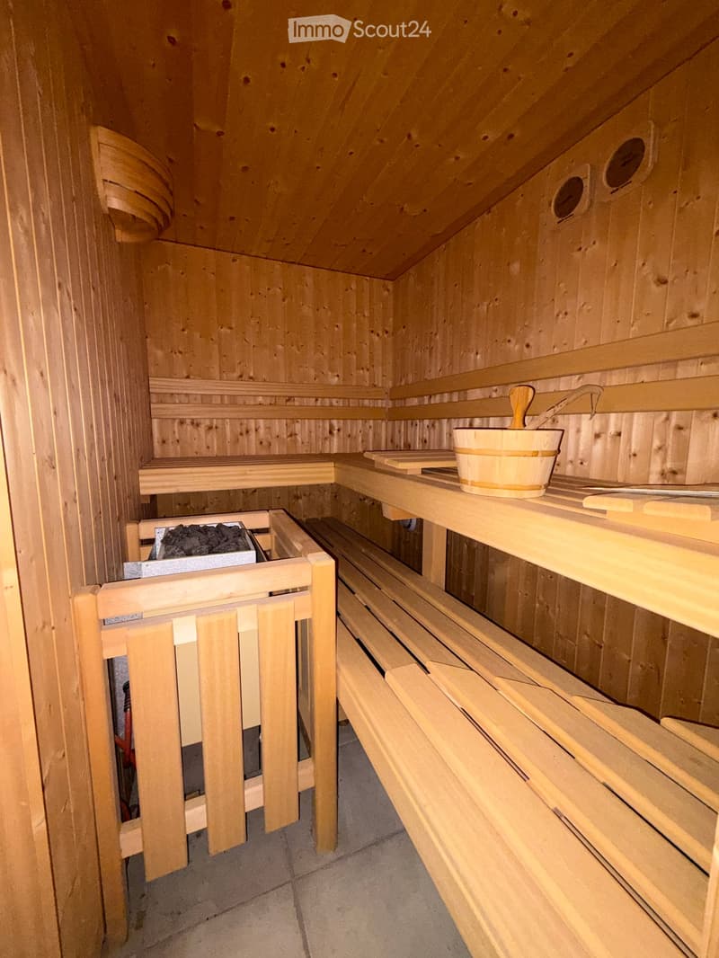 Wooden sauna with multiple benches, a bucket, and a paddle on a shelf.