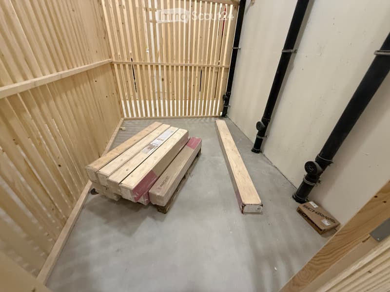Empty room with unfinished wooden walls, concrete floor, and scattered wooden planks and boxes.