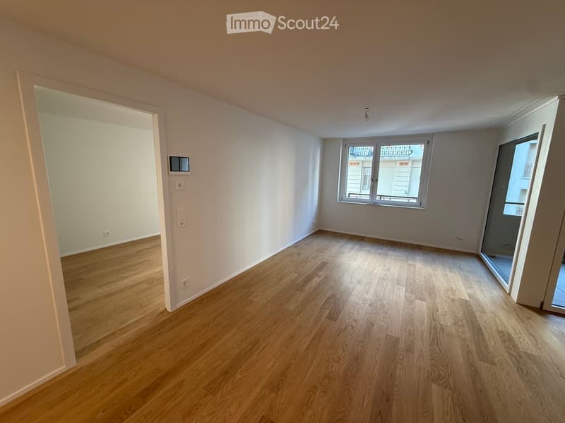 Empty room with wooden flooring, white walls, and large windows, featuring a door leading to a balcony.