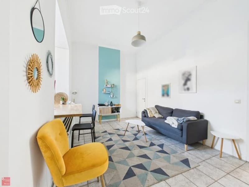 Bright living room with white walls, a blue accent wall, and a geometric patterned rug. Features a grey sofa, yellow armchair, coffee table, dining table with chairs, shelves, and decorative mirrors.