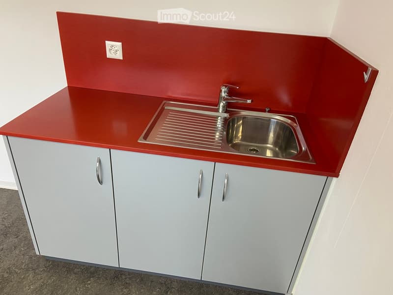 Modern kitchen with red countertop, stainless steel sink, and grey cabinets.