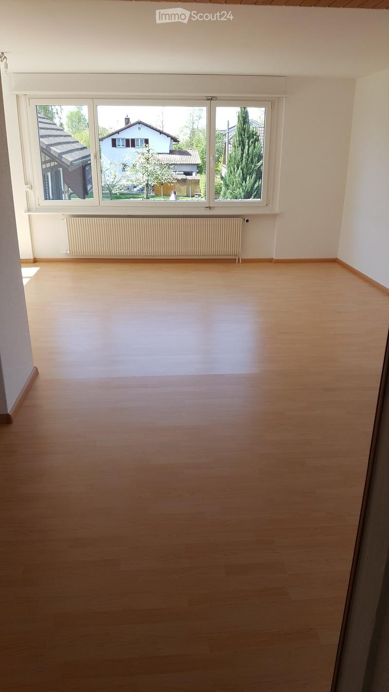 Empty room with wooden flooring, white walls, large windows, radiator, and visible outdoor view.