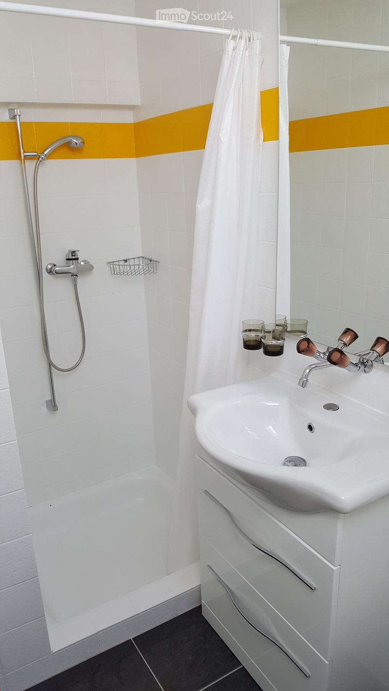 Modern bathroom with white tiles, a shower area, a sink with a faucet, and a white cabinet. The walls feature a yellow accent stripe, and a white shower curtain is visible.